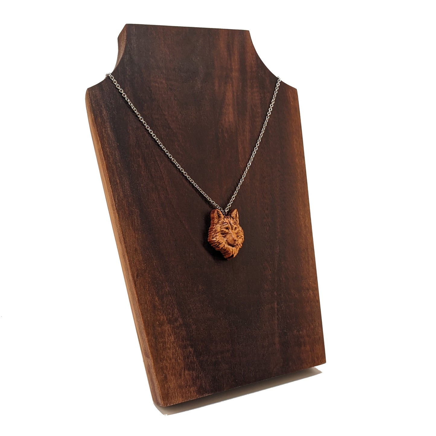 Wooden necklace pendant carved in the shaped of an wolf head. Made from hard maple wood. Hanging from a silver stainless steel chain against a dark walnut background.