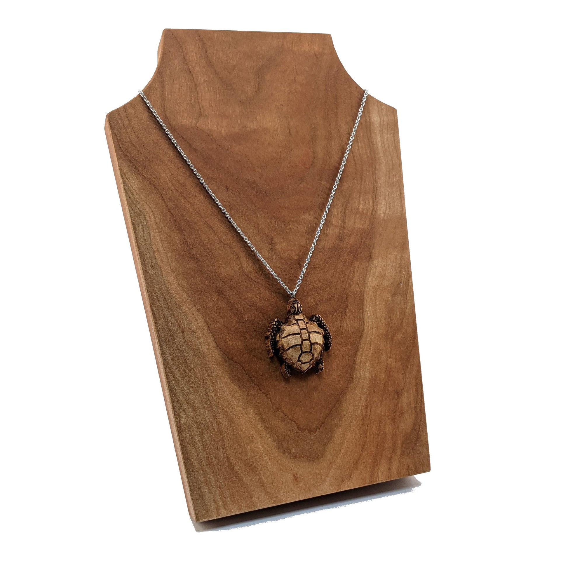 Wooden necklace pendant carved in the shape of a sea turtle. Made from hard maple wood. Hanging from a silver stainless steel chain against a cherry wood background.