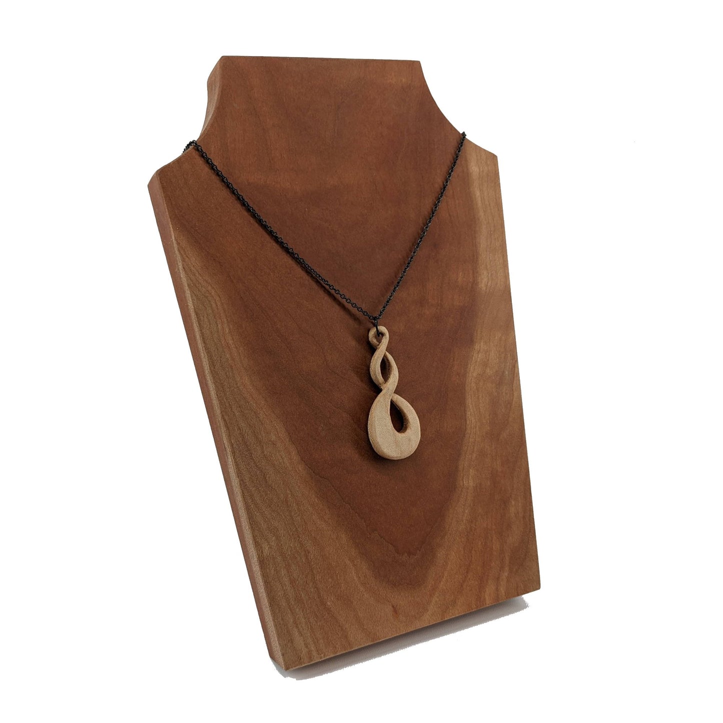 Wooden necklace pendant carved in the shape of a twisted infinity inspired symbol. Made from hard maple wood. Hanging from a black stainless steel chain against a cherry wood background.