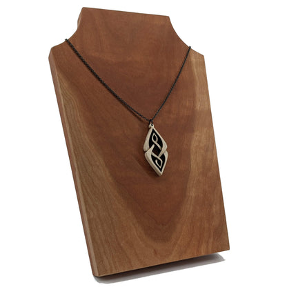 Wooden necklace pendant carved so that curving shapes weave into each other. Made from hard maple wood and hanging from a black chain against a cherry wood background.