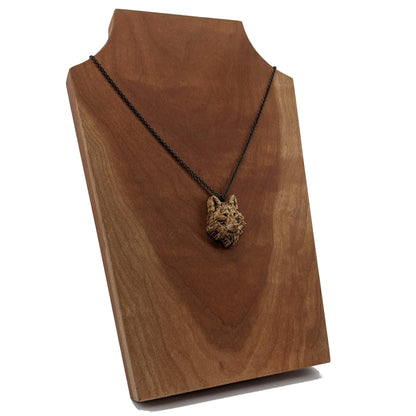 Wooden necklace pendant carved in the shaped of an wolf head. Made from hard maple wood. Hanging from a black stainless steel chain against a cherry wood background.