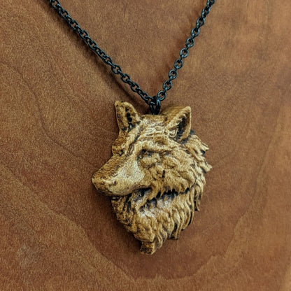 Wooden pendant necklace carved in the shape of a wolf head. The wolf faced to the side and made from hard maple wood. It hangs from a black stainless steel chain against a cherry wood background.