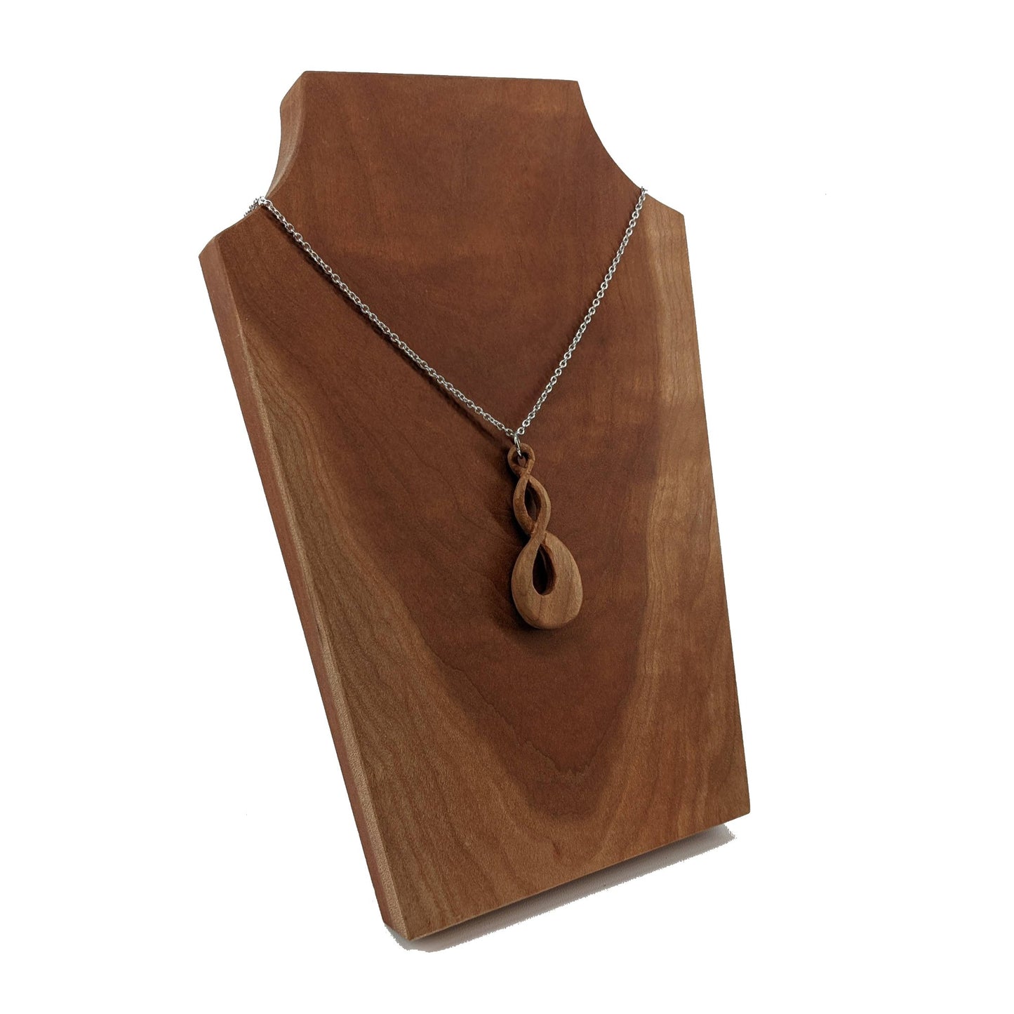 Wooden necklace pendant carved in the shape of a twisted infinity inspired symbol. Made from cherry wood. Hanging from a silver stainless steel chain against a cherry wood background.