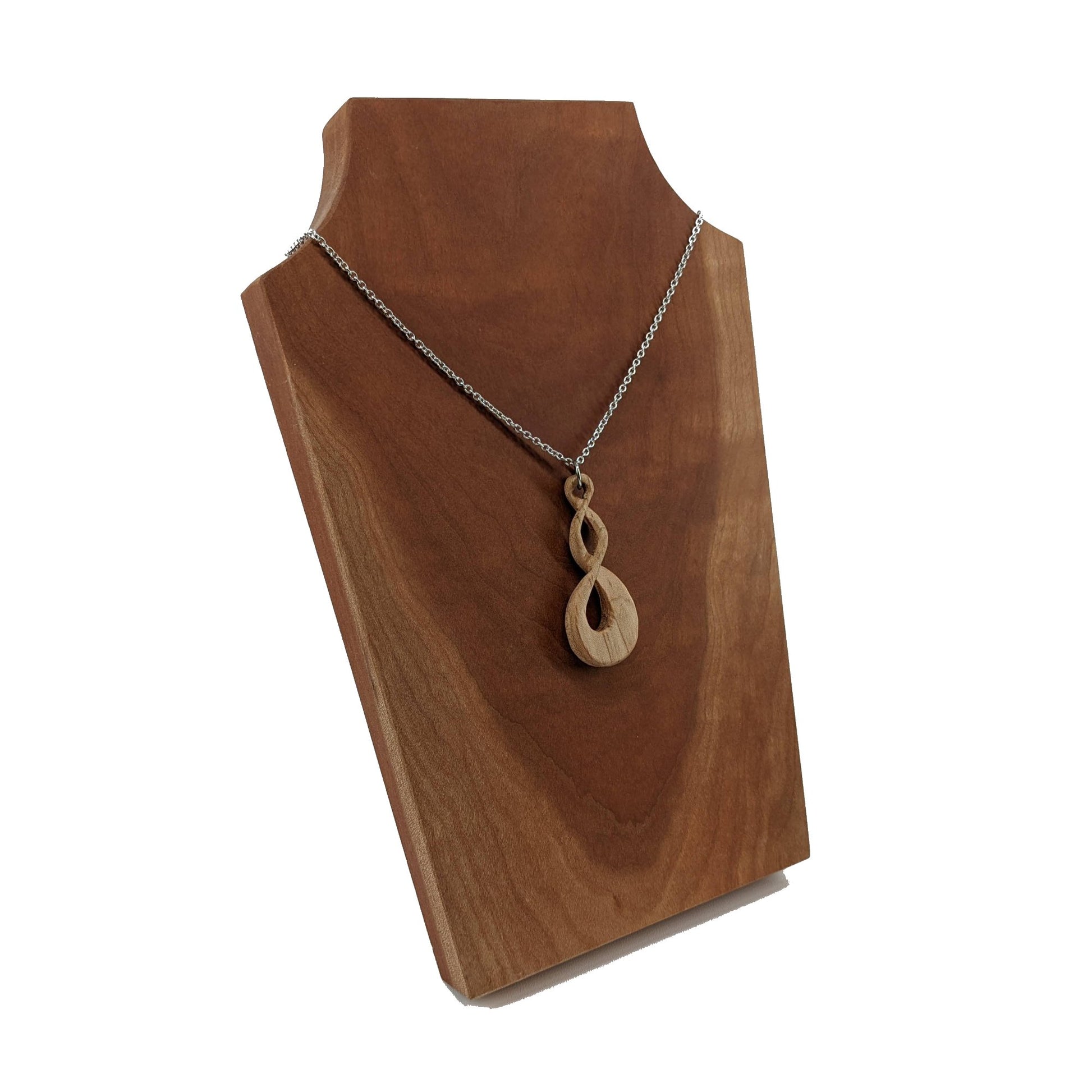 Wooden necklace pendant carved in the shape of a twisted infinity inspired symbol. Made from cherry wood. Hanging from a silver stainless steel chain against a cherry wood background.