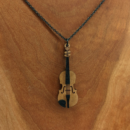 Wooden necklace pendant created in the shape of a miniature violin. Made from hard maple wood and hanging from a black stainless steel chain against a cherry wood background.