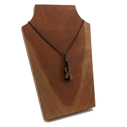 Wooden necklace pendant created in the shape of a miniature violin. Made from hard maple wood and hanging from a black stainless steel chain against a cherry wood background.