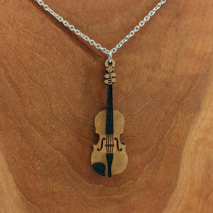 Wooden necklace pendant created in the shape of a miniature violin. Made from hard maple wood and hanging from a silver stainless steel chain against a cherry wood background.