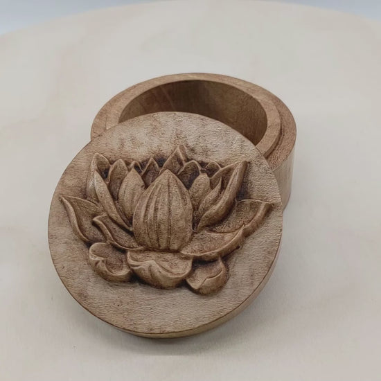 Round wooden box 3D carved with a side profile of a lotus flower. It has several layers of leaves closer to the bottom and layers of petals going up the flower to the pointed center. Made from hard maple wood stained brown against a white background rotating on a table.