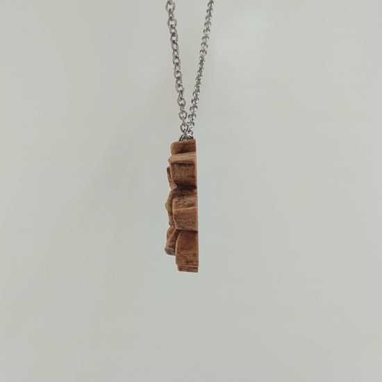 Wooden magnolia flower pendant carved in a realistic style from hard maple wood. Hanging from a silver stainless steel chain against a white background rotating on a table.