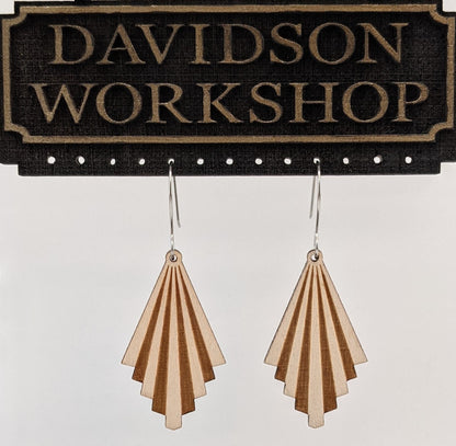 Pair of wooden earrings with silver stainless steel hooks hanging on a display. They are light and dark striped tiers in a triangular shape. Made from birch wood hanging from a model Davidson Workshop sign against a white background. (Close up View)