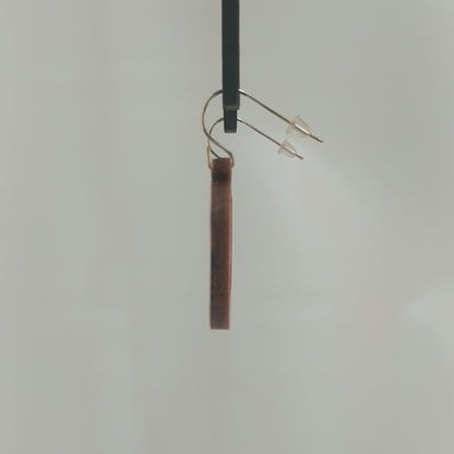 Pair of wooden earrings with silver stainless steel hooks. They are two toned light and dark brown miniature snare drums with drumsticks on top. Made from birch wood hanging and rotating against a white background.