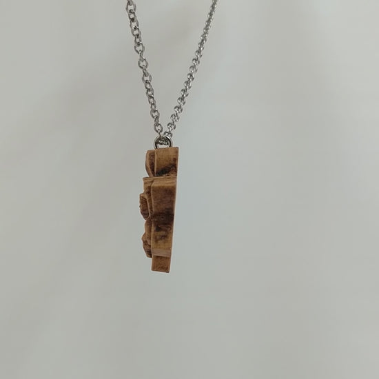 Wooden flower necklace pendant carved in the shape of a gardenia against. Made from hard maple and hanging from a silver stainless steel chain against a white background rotating on a table.