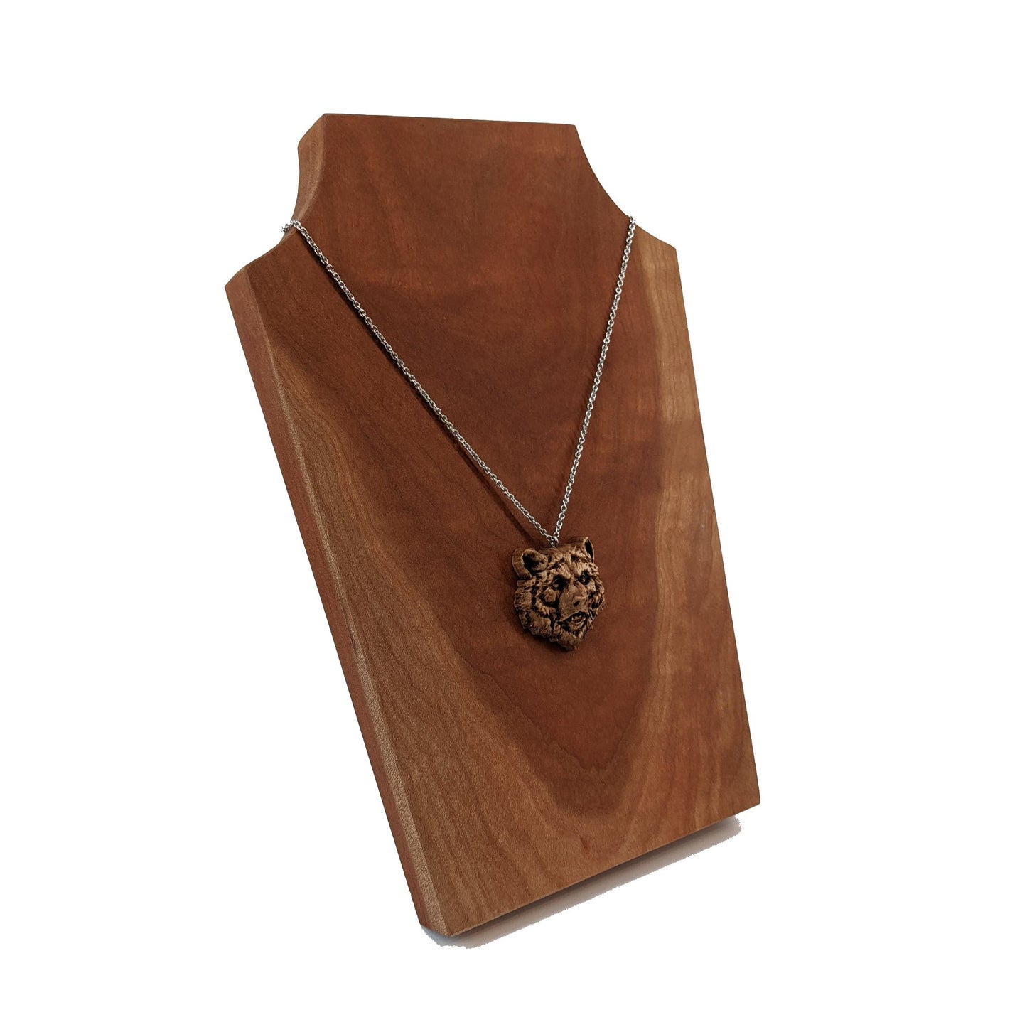 Wooden necklace pendant carved in the shape of a grizzly bears head. Made from hard maple wood. Hanging from a silver stainless steel chain against a cherry wood display.