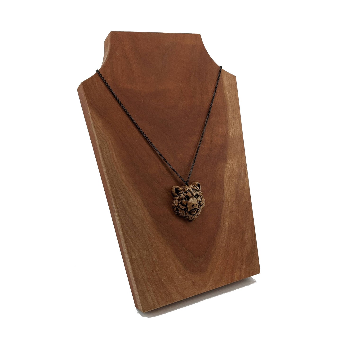 Wooden necklace pendant carved in the shape of a grizzly bears head. Made from hard maple wood. Hanging from a black stainless steel chain against a cherry wood display.