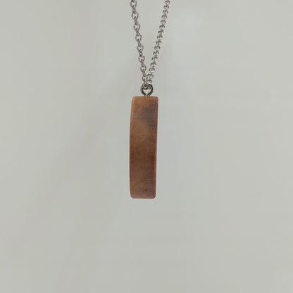 Wooden necklace pendant carved in the shape of a monkey with his hand on his chin. Made from hard maple wood and hanging from a silver stainless steel chain against a white background rotating on a table.