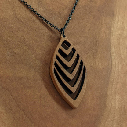 Wooden necklace pendant cut into a teardrop shape with a chevron pattern cut throughout it. Made from cherry and hanging from a black stainless steel chain against a cherry background.