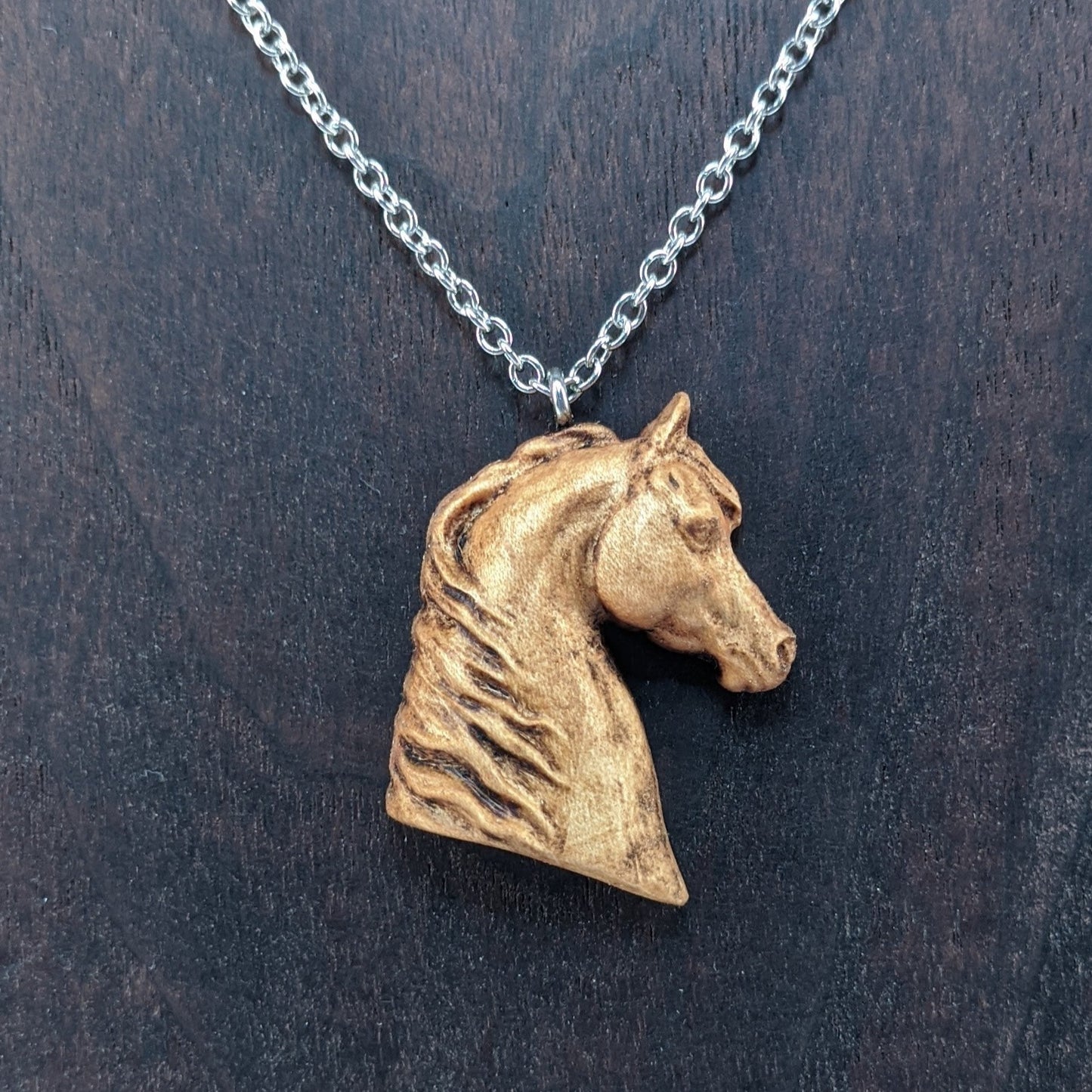 Wooden pendant realistically carved in the shape of a horse. Made form hard maple and hung from a silver stainless steel chain against a dark walnut background.