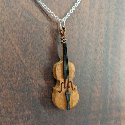 Wooden necklace pendant created in the shape of a miniature cello stand up bass. Made from cherry wood and hanging from a silver stainless steel chain against a dark walnut background.