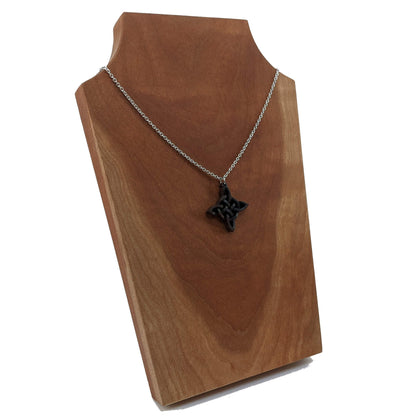 Wooden necklace pendant created in the style of a Celtic woven cross. Made from dark walnut.  Hanging from a silver stainless steel chain against a cherry wood background.