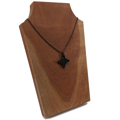 Wooden necklace pendant created in the style of a Celtic woven cross. Made from dark walnut.  Hanging from a black stainless steel chain against a cherry wood background.