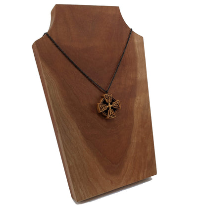 Wooden necklace pendant created in the shape of a Celtic cross. Made from hard maple wood and hanging from a black stainless steel chain against a cherry wood display.