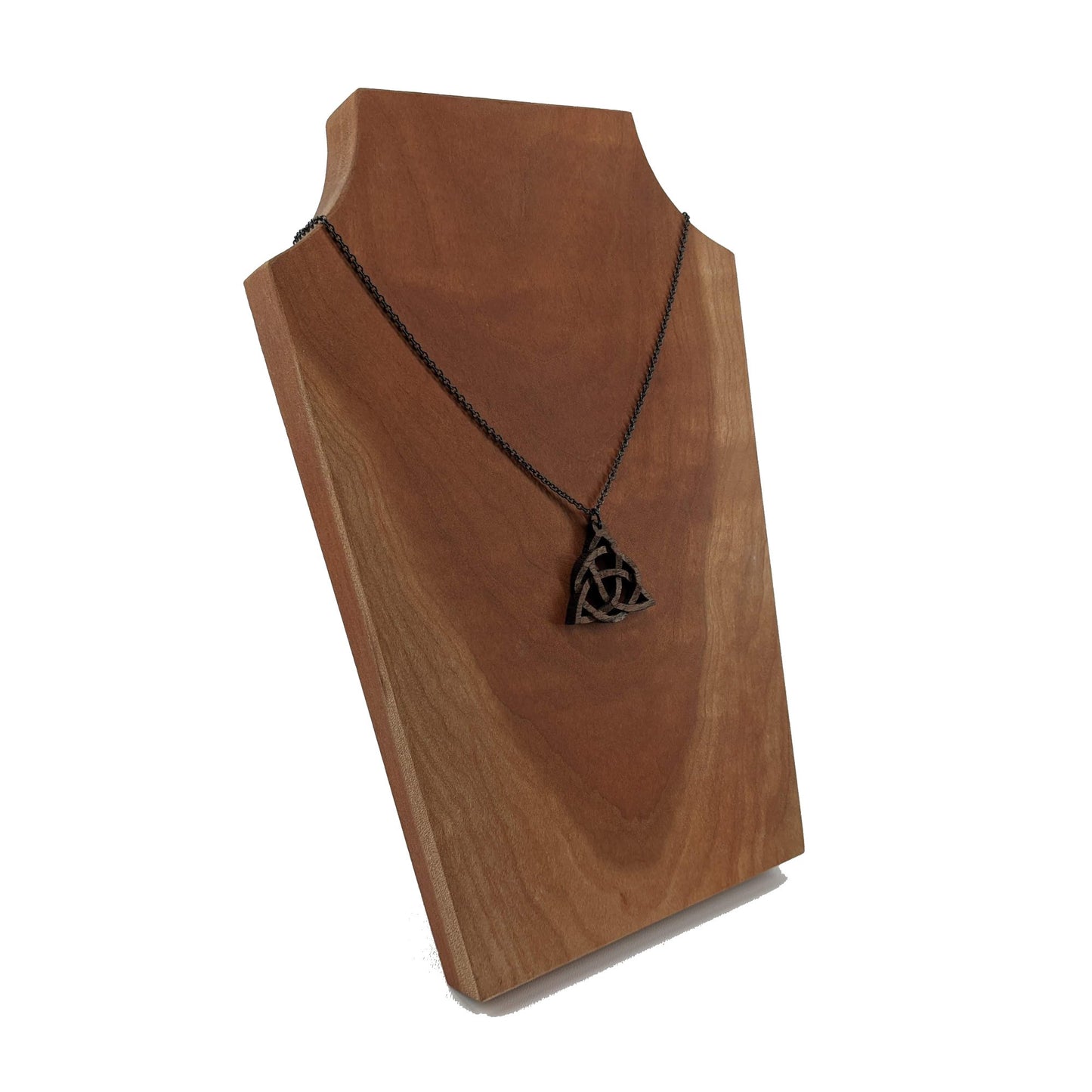 Wooden necklace pendant created in the style of a Celtic woven trinity symbol. Made from dark walnut. Hanging from a black stainless steel chain against a cherry wood background.