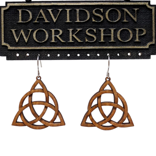 Pair of wooden earrings with silver stainless steel hooks. They are Celtic carved in a woven pattern forming 3 points with a center circle. Made from hard maple hanging from a model Davidson Workshop sign against a white background. (Close up View)