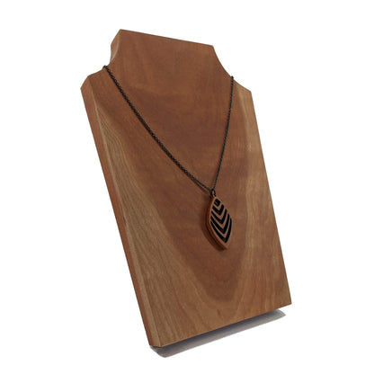 Wooden necklace pendant cut into a teardrop shape with a chevron pattern cut throughout it. Made from cherry and hanging from a black stainless steel chain against a cherry background.