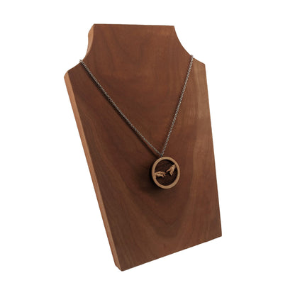 Round wooden necklace pendant carved in the shape of 2 hands reaching out to touch each other. The hands are carved from light maple wood overlayed on a dark walnut base. Hanging from a silver stainless steel chain against a cherry wood background.