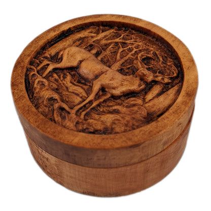 Round wooden box 3D carved with a buck deer standing in a forest. It stands in small grassy knolls in front of trees that have thin branches sticking out in every direction. Made from hard maple wood with a brown stain against a white background.