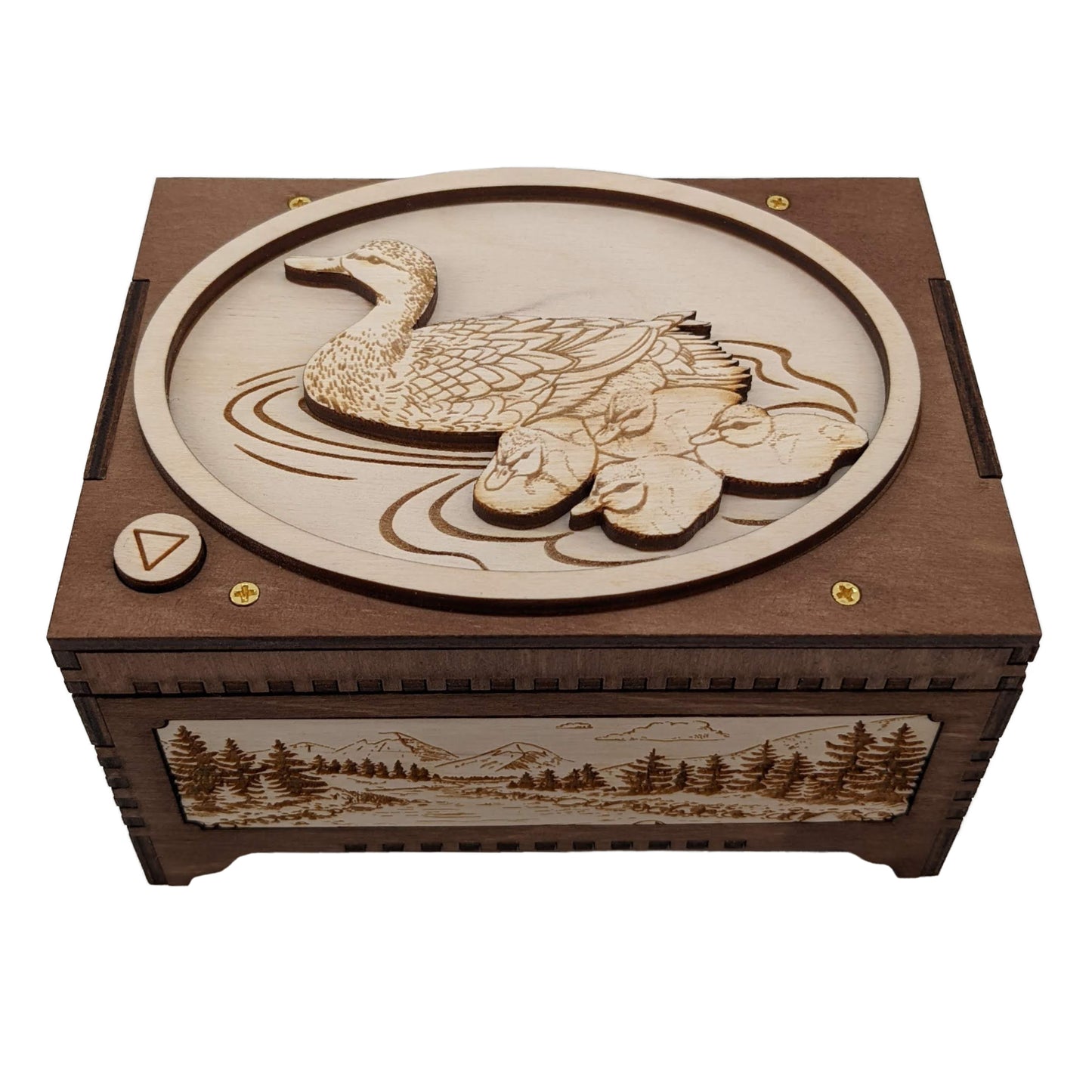 Front view of a mother duck and ducklings music box, showing a peaceful mountain, trees, and river scene engraved on a decorative panel in the front of the box, as well as the engraved mother duck and ducklings swimming in water on top of the box.