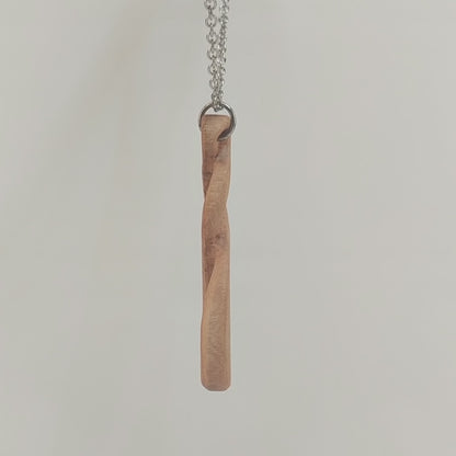 Wooden necklace pendant carved in the shape of a twisted infinity inspired symbol. Made from cherry wood. Hanging from a silver stainless steel chain against a white background rotating on a table.