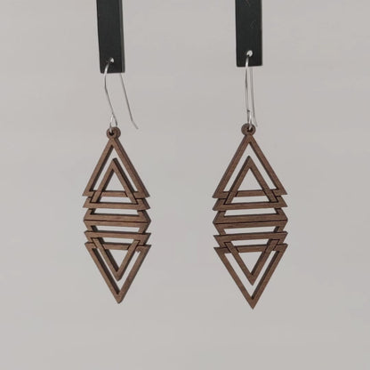 Pair of wooden earrings with silver stainless steel hooks. They are multiple brown triangles overlapping and mirrored to make a diamond shape. Made from birch wood hanging and rotating against a white background.