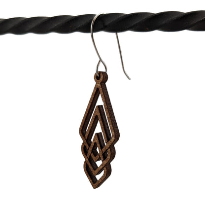 Laser cut wood earring hanging from a large loop earring hook, hanging on a twisted black iron bar.  Set against a white background.