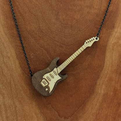 Electric guitar shaped wooden necklace pendant. Made from birch wood and stained dark brown. Hanging from a black stainless steel chain against a cherry wood background.