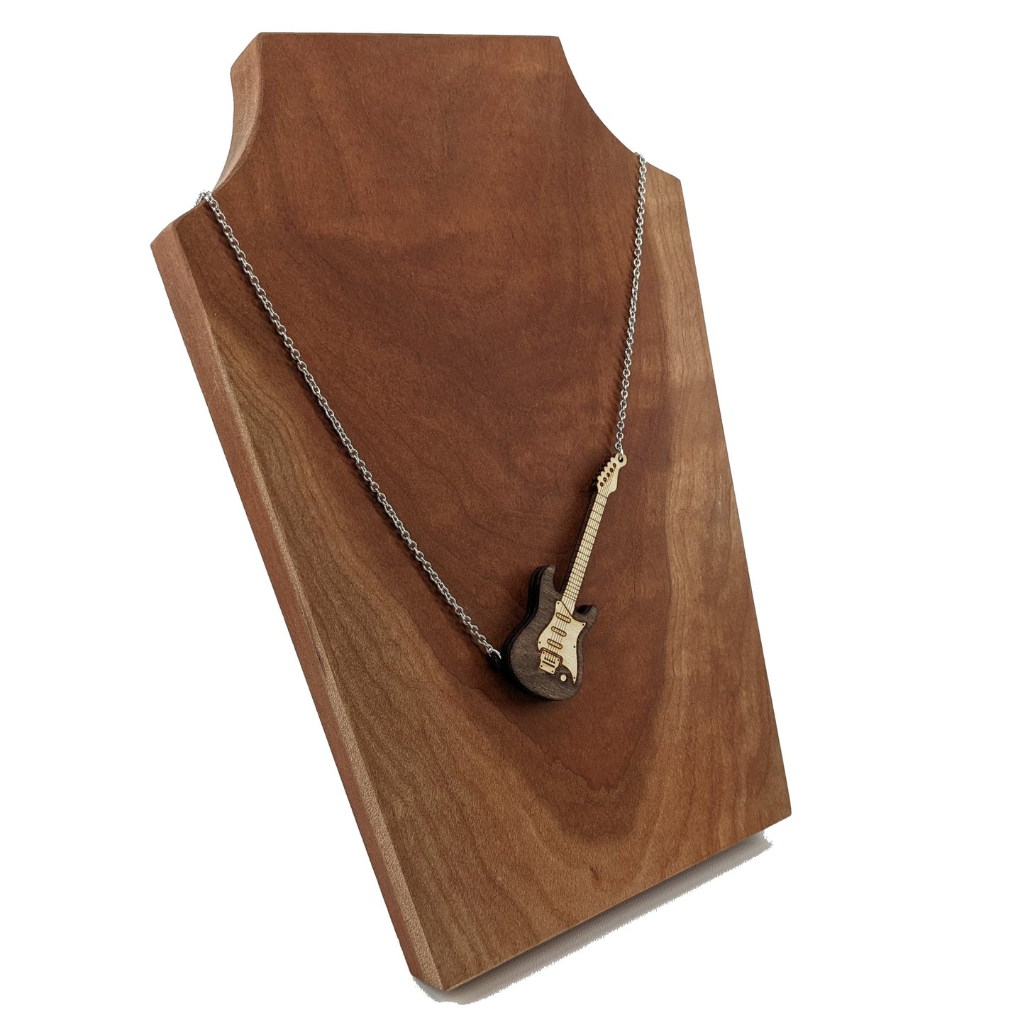 Electric guitar shaped wooden necklace pendant. Made from birch wood and stained dark brown. Hanging from a silver stainless steel chain against a cherry wood background.