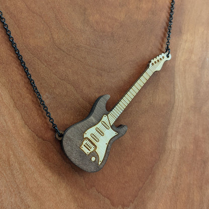 Electric guitar shaped wooden necklace pendant. Made from birch wood and stained dark brown. Hanging from a black stainless steel chain against a cherry wood background.