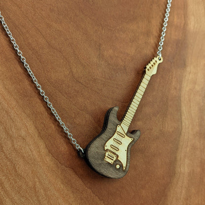 Electric guitar shaped wooden necklace pendant. Made from birch wood and stained dark brown. Hanging from a silver stainless steel chain against a cherry wood background.