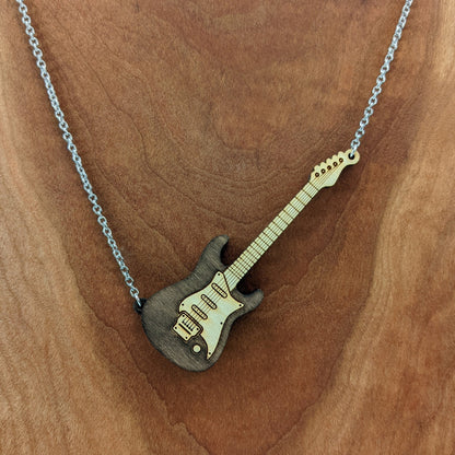 Electric guitar shaped wooden necklace pendant. Made from birch wood and stained dark brown. Hanging from a silver stainless steel chain against a cherry wood background.