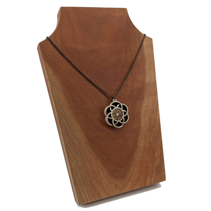 Wooden necklace pendant inspired by a flower of life including 6 interlinking circles creating a flower in the center. Carved from hard maple wood. Hanging from a black stainless steel chain against a cherry wood background.