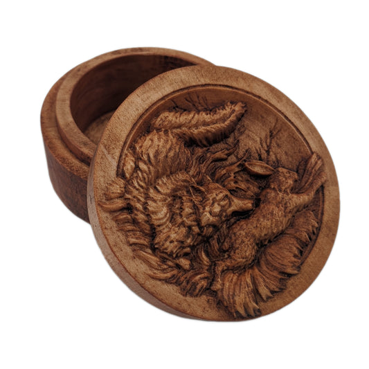 Round wooden box 3D carved with a foreground of a fox chasing a rabbit through tall plush grass in a clearing just outside a forest. Where there are the tops of bare thin trees. Made from hard maple wood with a brown stain against a white background.