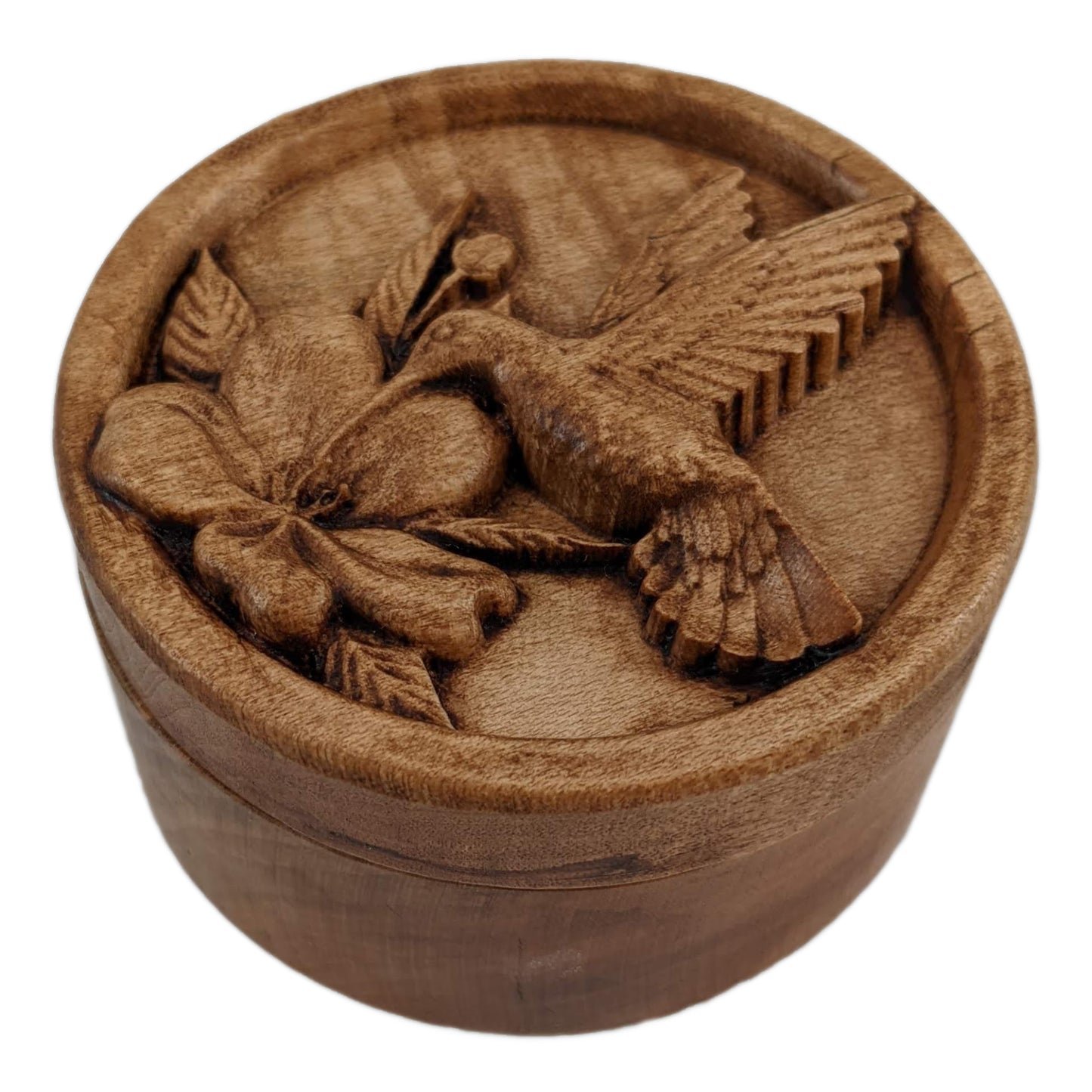 Round wooden box 3D carved with a recessed hummingbird hovering and drinking nectar from a flower. It is facing to the left with its delicate wings aflutter as it leans in to drink. Made from hard maple wood stained brown against a white background.