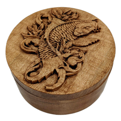 Round wooden box 3D carved with a koi fish surrounded by leaves and filigree designs. It has flowing whiskers, a sharp back fin and intricately carved scales down to its wide tail. Made from hard maple wood stained brown against a white background.