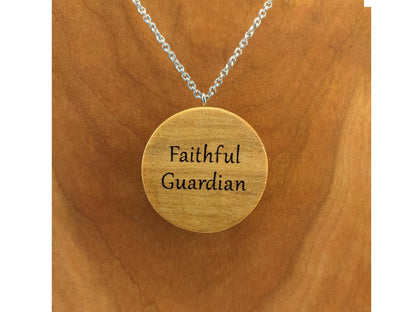 Round wooden necklace pendant engraved with personalized wording on the back. Hanging from a silver stainless steel chain against a cherry wood background.