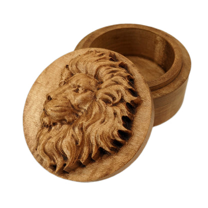 Round wooden box 3D carved with a side profile of a lions face. It has a serious look in its brow with a closed mouth facing to the left with a large bushy mane surrounding its face. Made from hard maple wood stained brown against a white background.