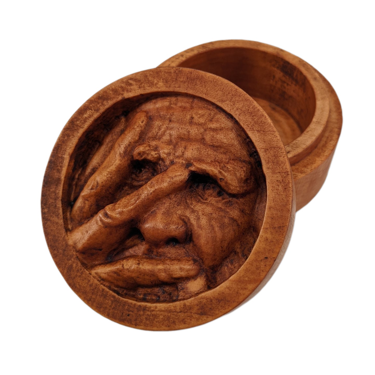 Round wooden box 3D carved with a recessed carving of an old mans face with many wrinkles and large eyebrows, with his fingers spread across and covering the right side of his face. Made from hard maple wood stained brown against a white background.
