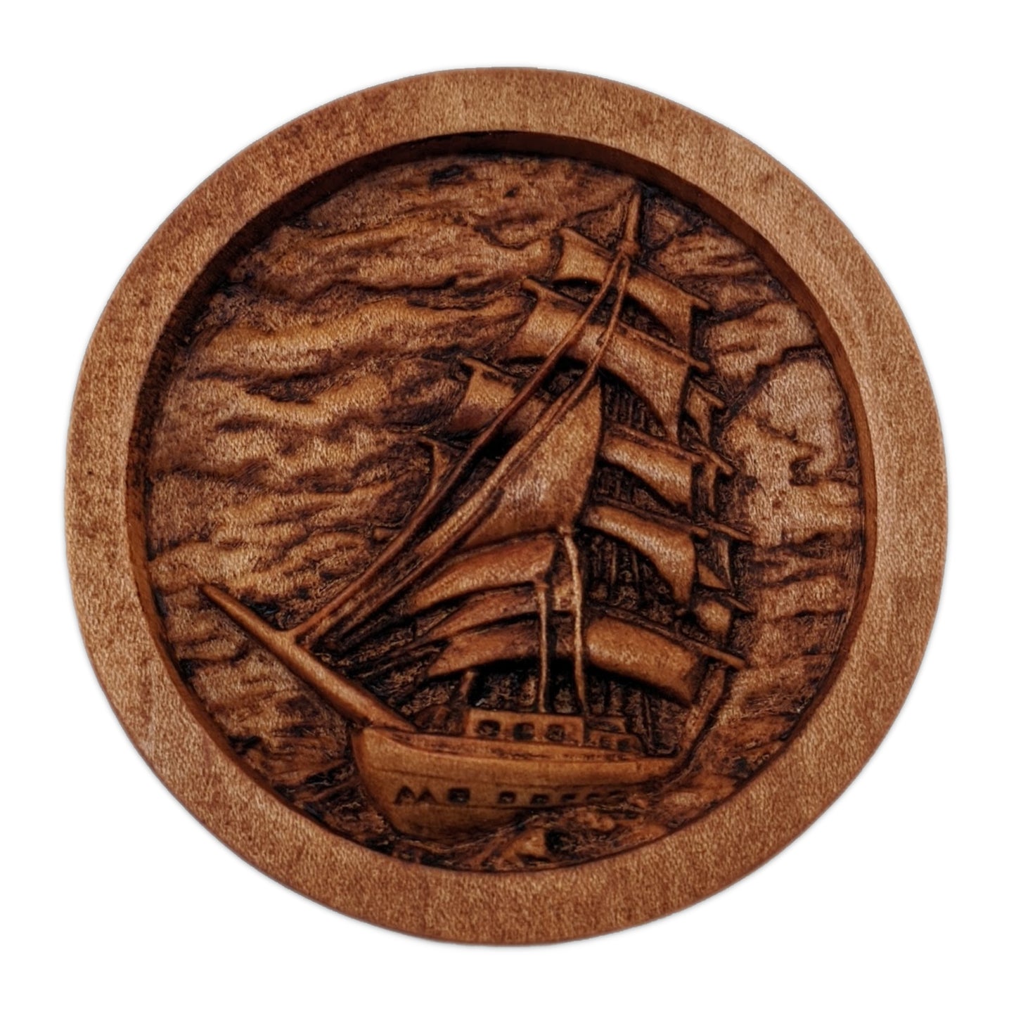 Round wooden box 3D carved with a large sailboat on the sea. It has multiple sails all pulled taught with ropes hanging all around. The background is a cloudy sky and rolling waves. Made from hard maple wood stained brown against a white background.