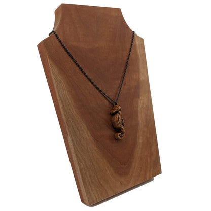 Wooden pendant necklace carved in the shape of sea horse. Made from hard maple and hanging from a black stainless steel chain against a white background.