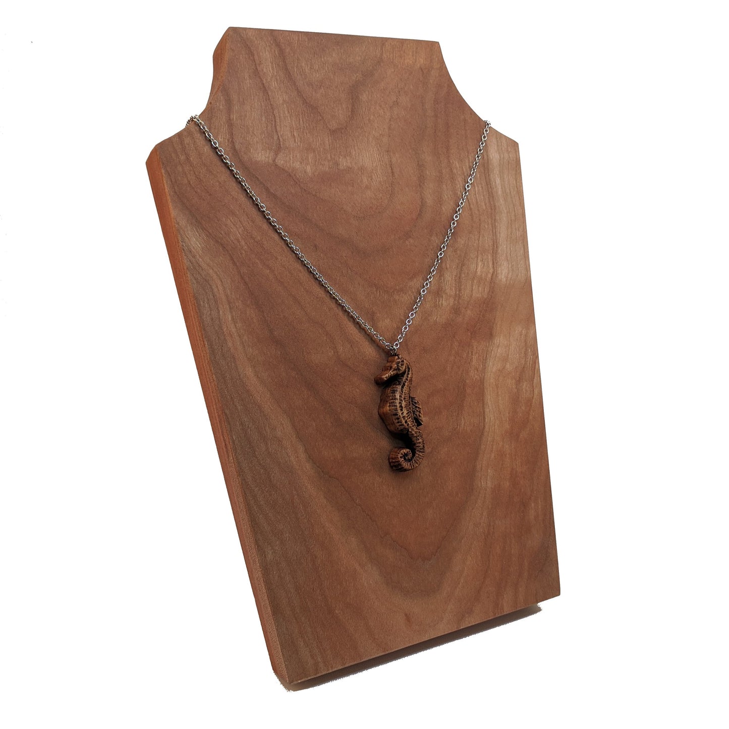 Wooden pendant necklace carved in the shape of sea horse. Made from hard maple and hanging from a silver stainless steel chain against a cherry wood background.