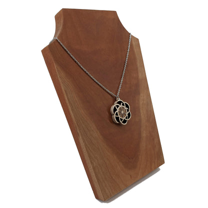 Wooden necklace pendant inspired by a flower of life including 6 interlinking circles creating a flower in the center. Carved from hard maple wood. Hanging from a black stainless steel chain against a cherry wood background.